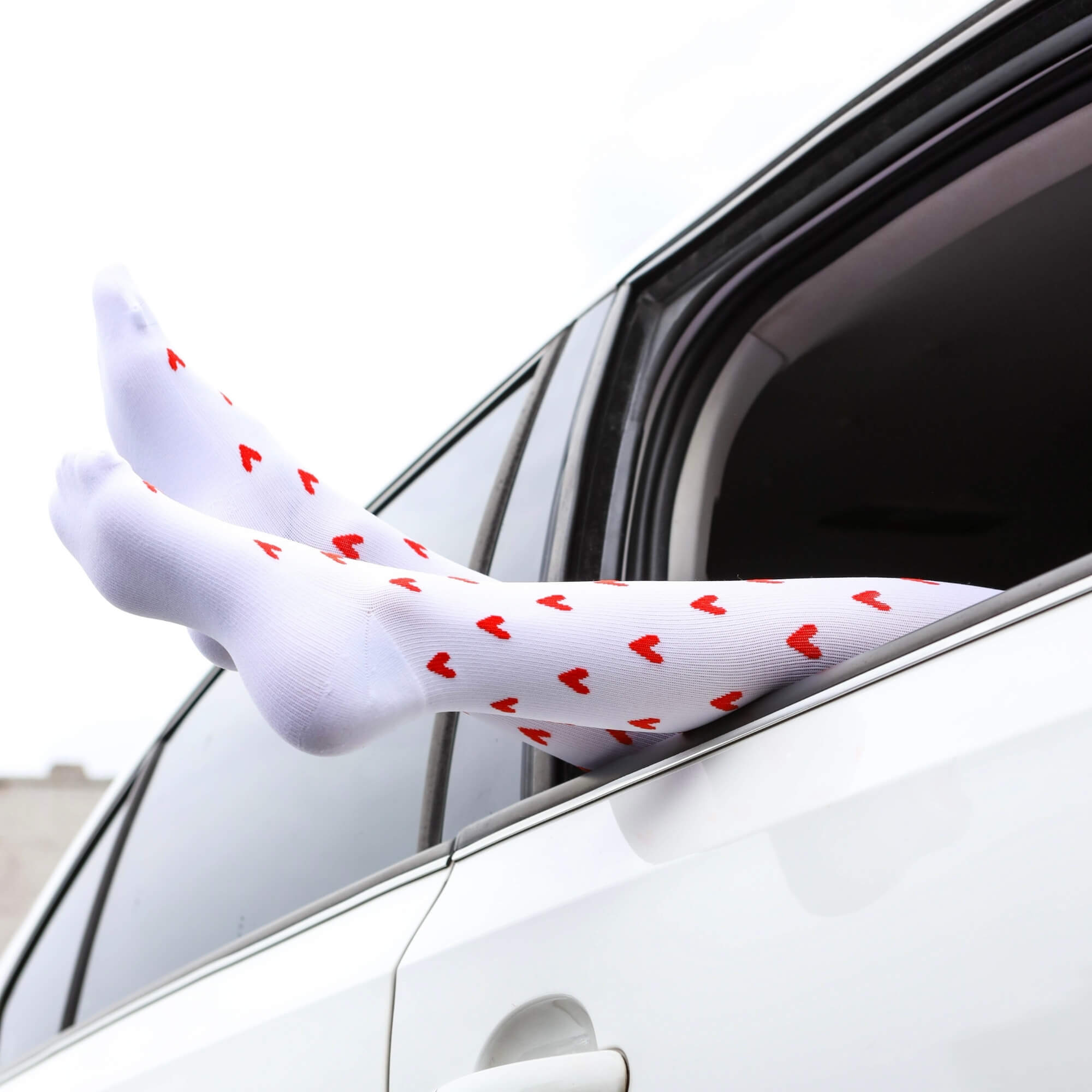 Legs with white compression socks with red heart patterns sticking out window