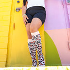 Woman wearing leopard print compression socks leaning on wall