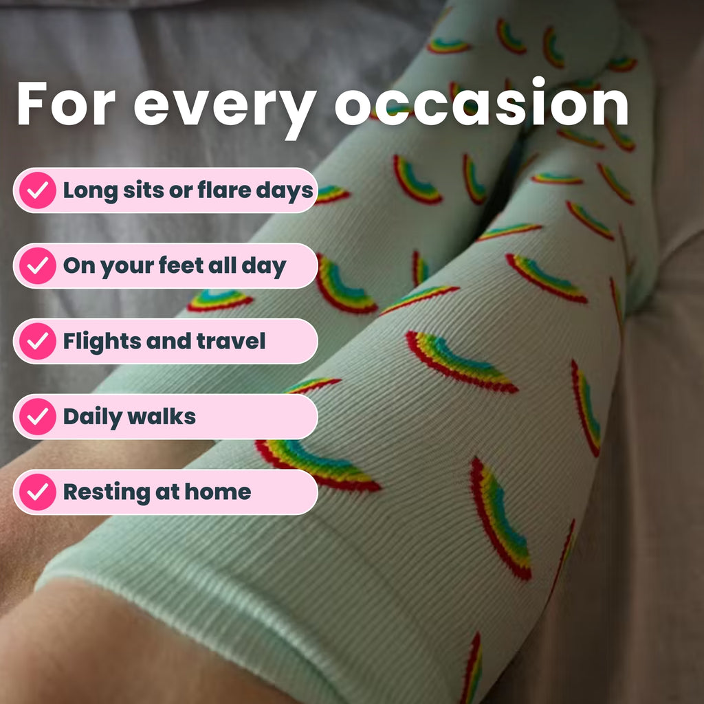 Legs wearing light blue compression socks with rainbow patterns on bed