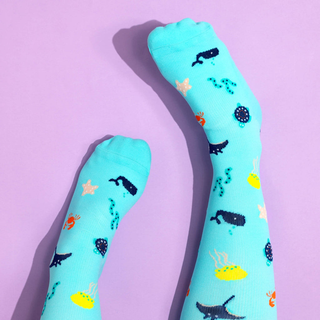 Teal compression socks with sea themed patterns on a pink background